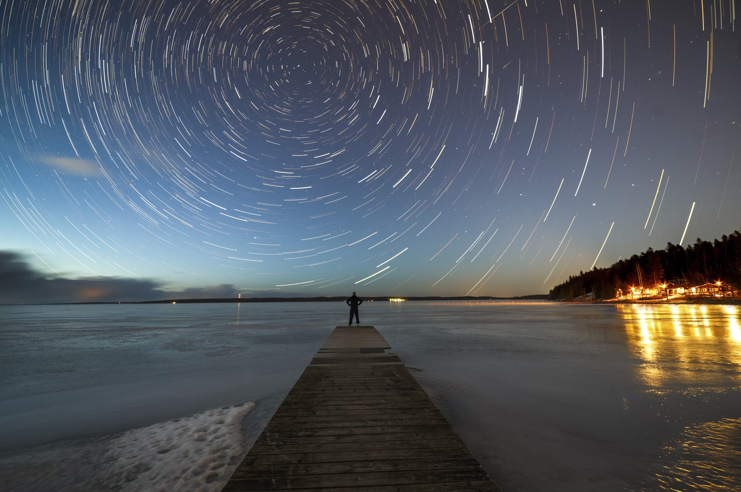 a person walking on a dock with a bright light in the sky
